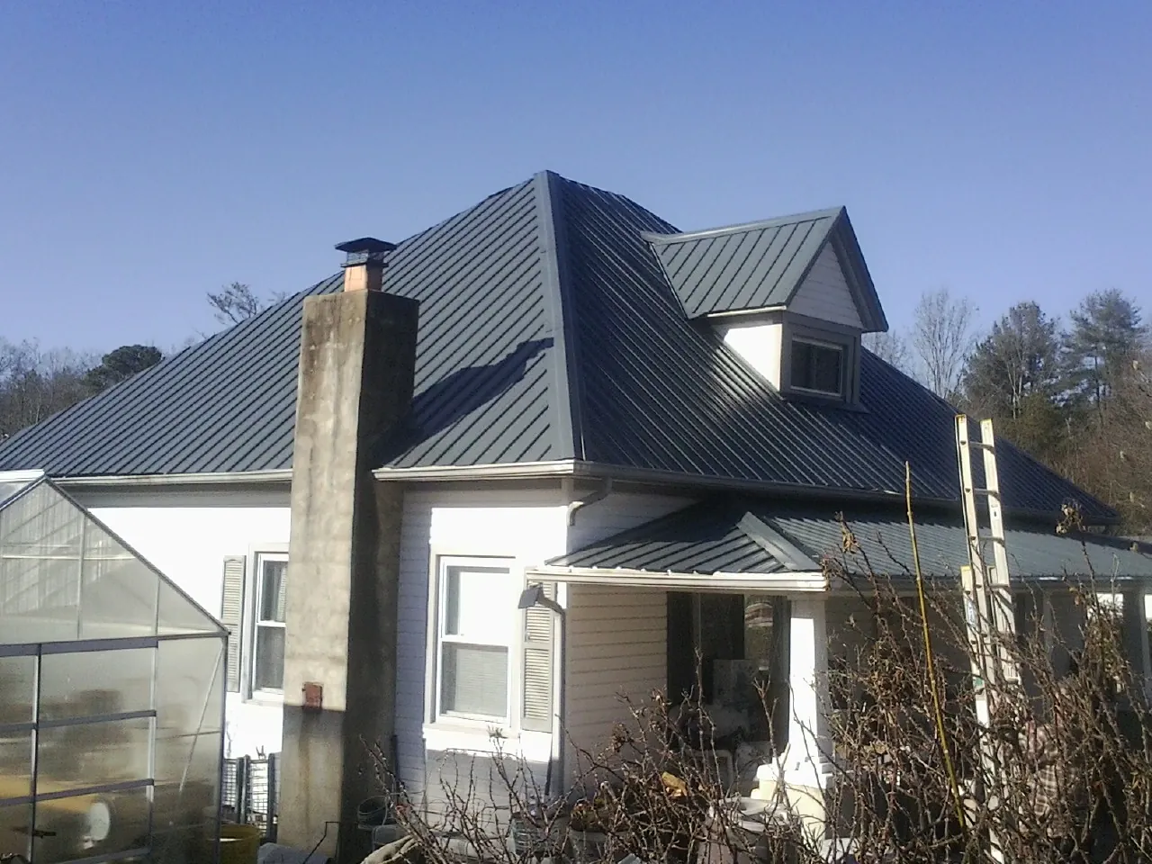 Dark blue standing seam metal roof on a white farmhouse with dormer — Slate & Tile Roof Repair by Roofing Brothers in Ratliff City