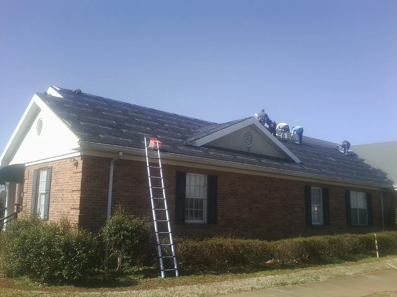 Crew tearing shingles off a brick ranch roof with a ladder set — Metal Roof Repair work by our crew in Ratliff City