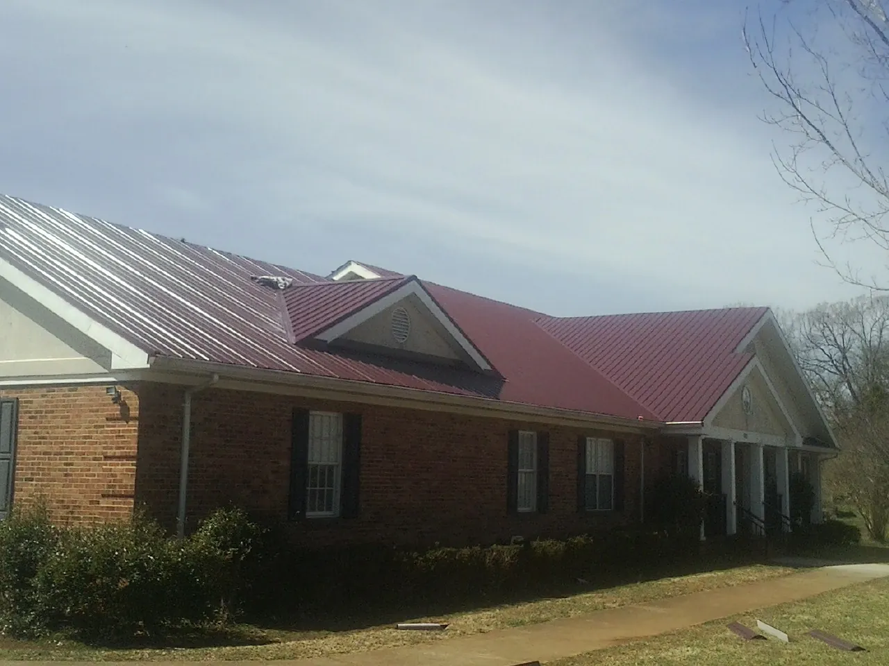 Red metal roof with gabled entries on a long brick building, from a Hail Damage Roof Repair job in Ratliff City