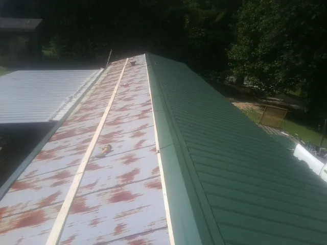Old rusted panels beside newly installed green metal roofing — Wind Damage Roof Repair by Roofing Brothers in Ratliff City
