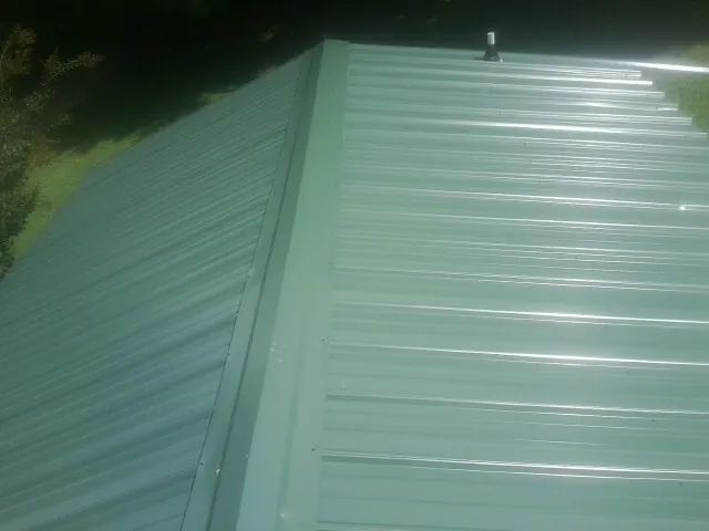 New green metal panels meeting at the ridge of a roof — Flat Roof Repair work by our crew in Ratliff City