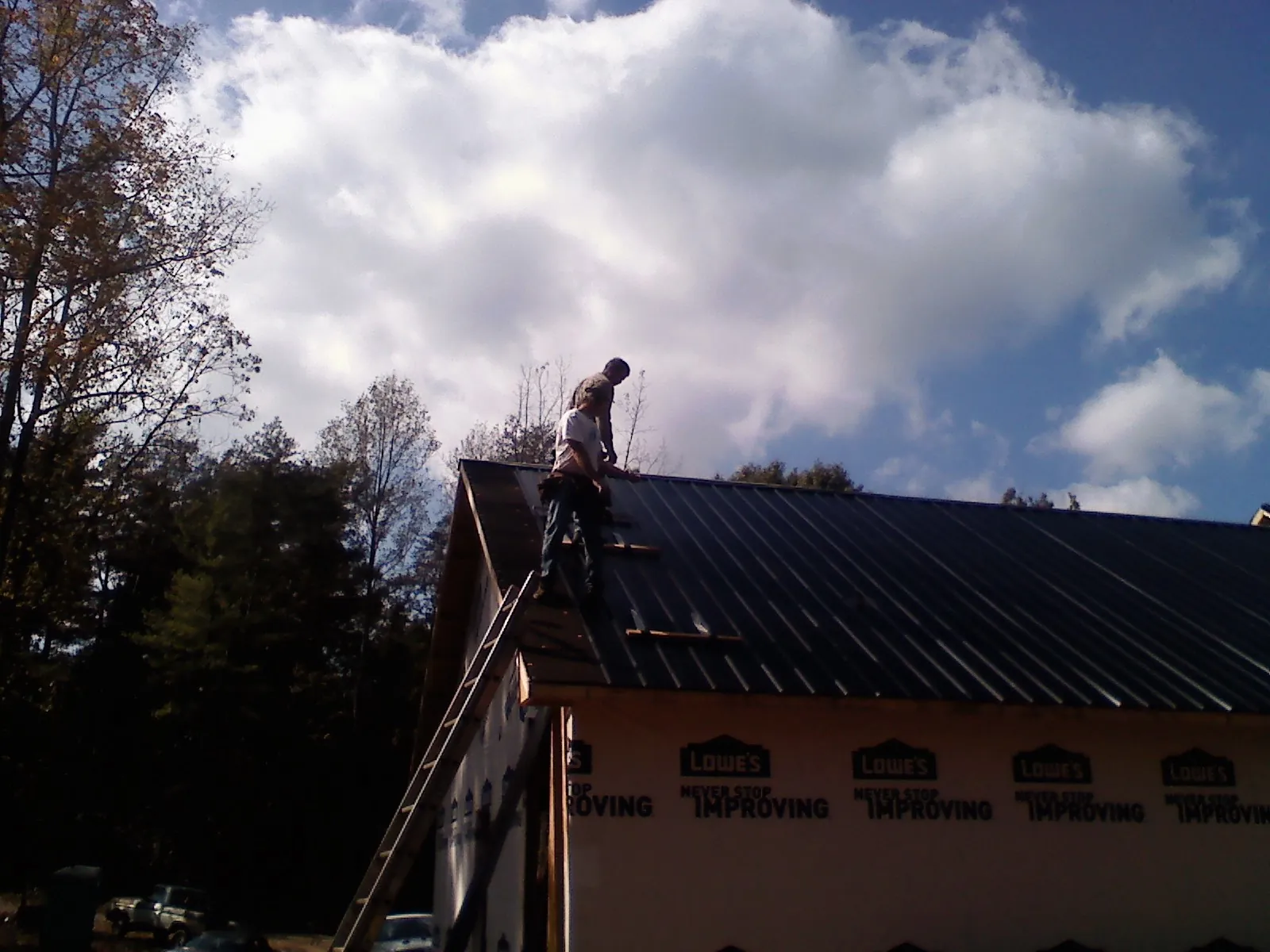 Roofer fastening dark metal panels high against a cloudy sky, from a Roof Inspection job in Ratliff City