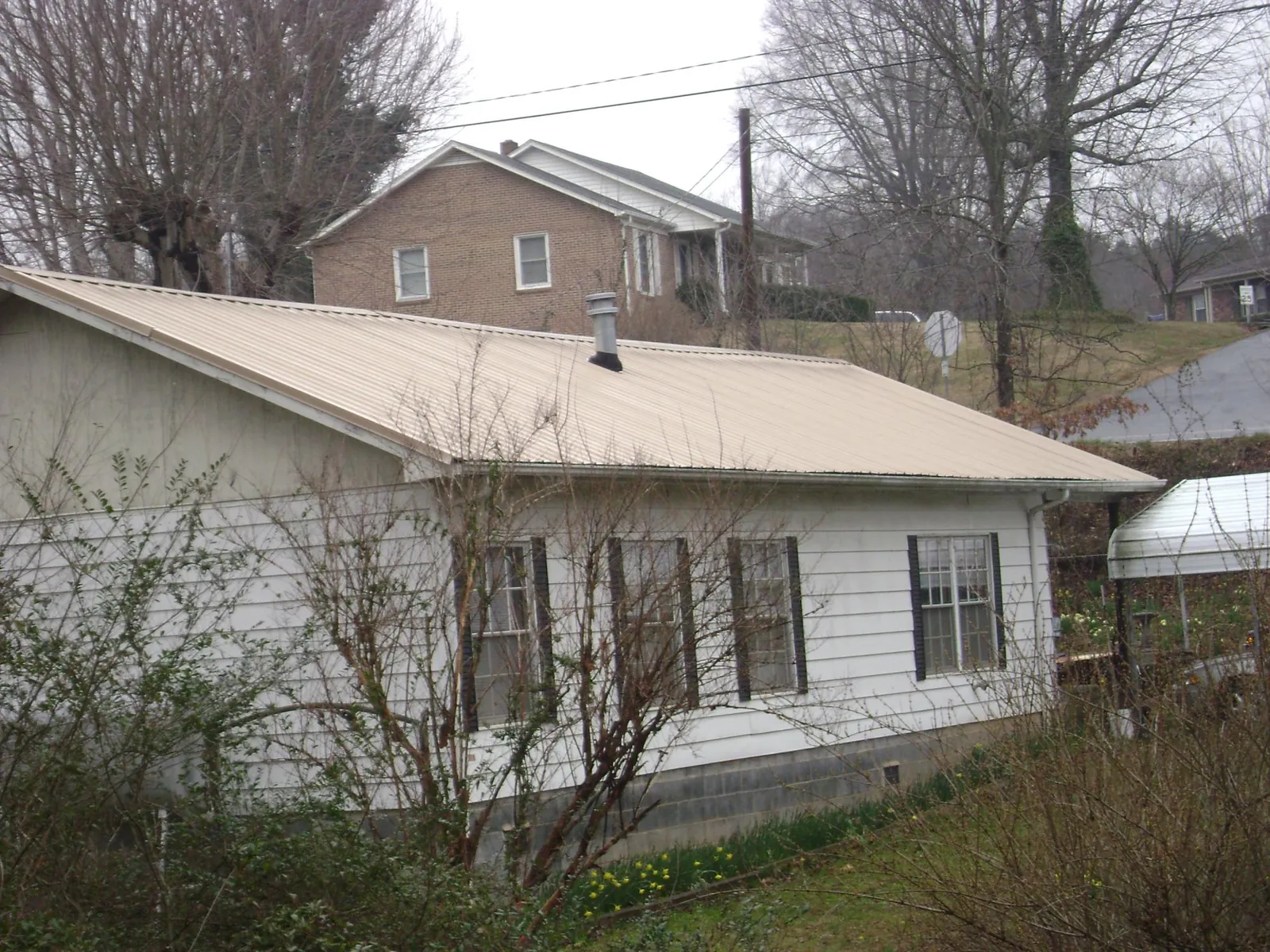 Tan metal roof on a white sided house set into a hillside — Commercial Roofing by Roofing Brothers in Ratliff City